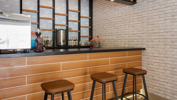 A bar area with a brick wall, wooden stools, and a counter with bottles and a coffee machine. - RedDoorz near Mall SKA Pekanbaru (Pekanbaru)