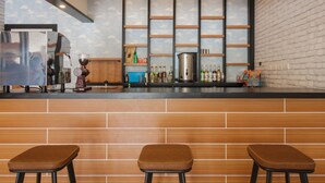 A bar area with a brick wall, wooden stools, a coffee machine, and shelves with bottles. - RedDoorz near Mall SKA Pekanbaru (Pekanbaru)