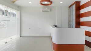 A reception area with a white and wooden reception desk, a glass wall, and a ceiling with recessed lighting. - RedDoorz near Mall SKA Pekanbaru (Pekanbaru)