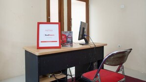 Un escritorio con un monitor de computadora, una silla y un letrero que indica una colaboración con RedDoorz.