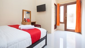 Habitación de hotel con cama, televisor, espejo, ventana con cortinas y puerta.