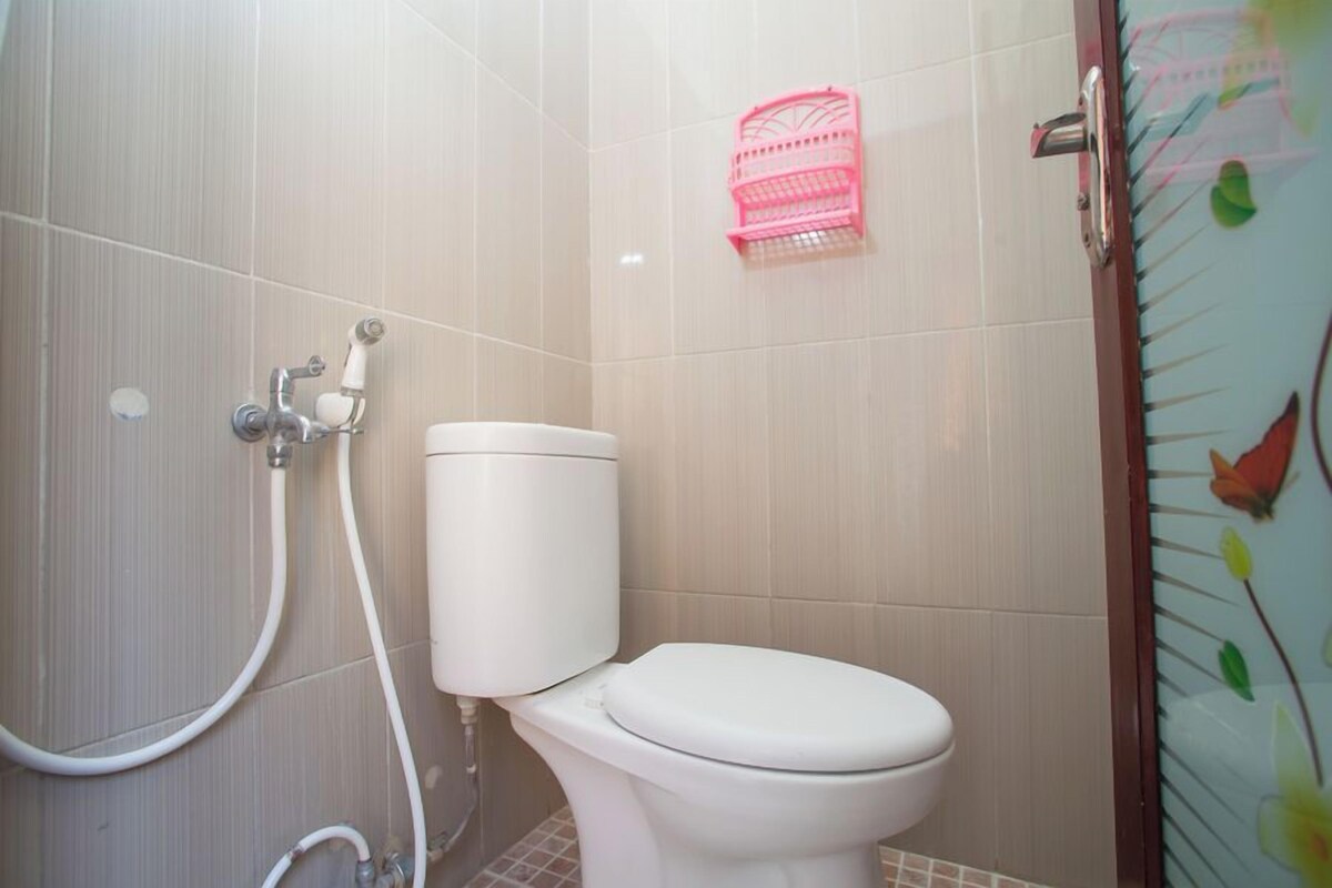 A bathroom with a toilet, a shower, and a pink basket on the wall.