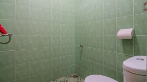 A bathroom with green tiles, a toilet, a shower, and a towel rack. - RedDoorz near Politeknik Negeri Medan (Medan)