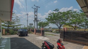 A gated parking area with a red scooter, a black car, and a yellow building in the background. - RedDoorz near Politeknik Negeri Medan (Medan)