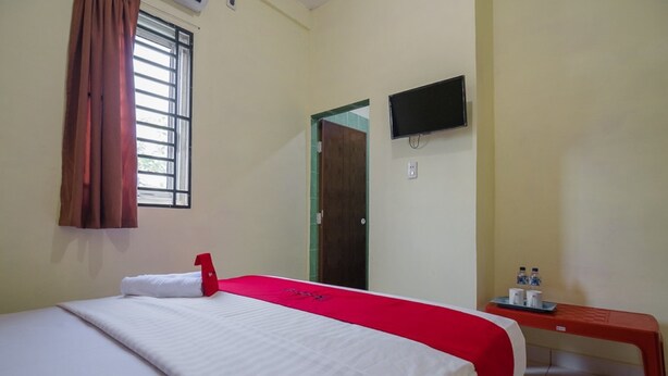 A hotel room with a bed, a TV mounted on the wall, a window with curtains, and a small table with water bottles. - RedDoorz near Politeknik Negeri Medan (Medan)
