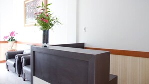 Ein Empfangsbereich mit dunklem Empfangstresen, zwei Ledersofas, einer Blumenvase und einem gerahmten Bild an der Wand.