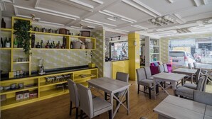 Ein Restaurantinneres mit gelb-weißer Einrichtung, Holztischen und einer Bar mit Regalen.