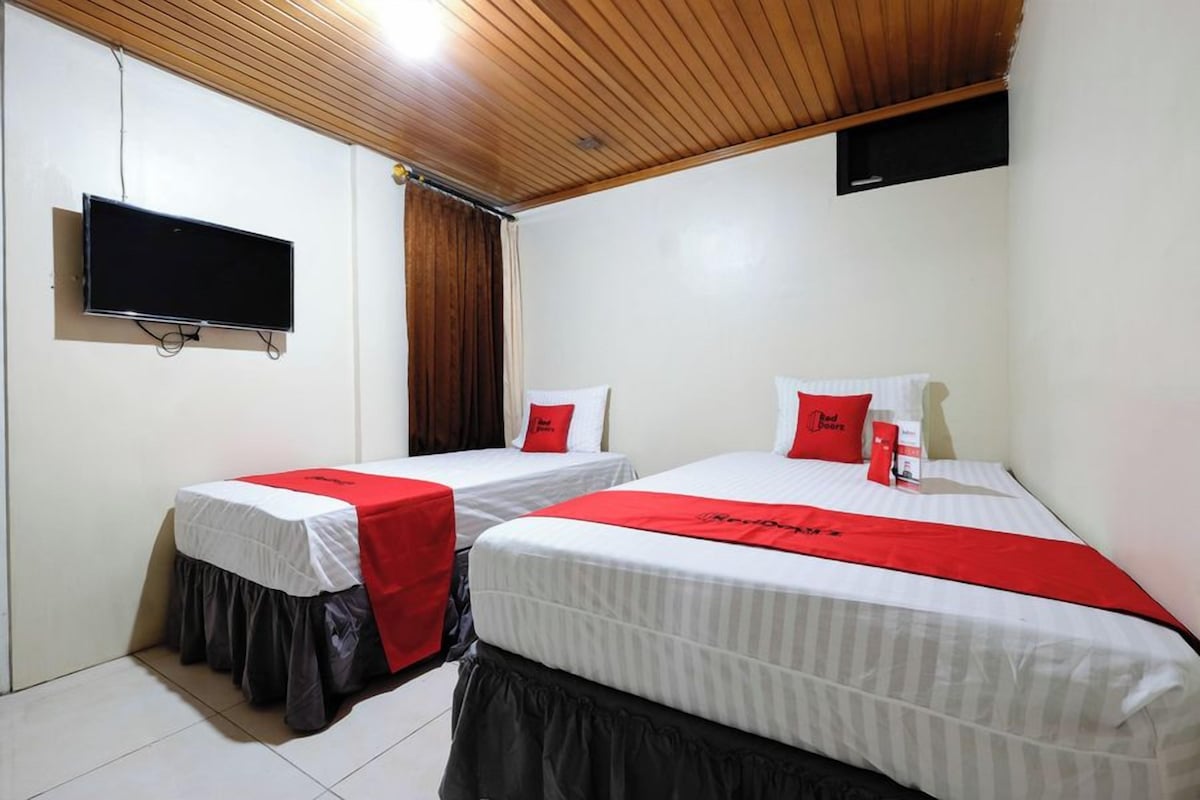 A hotel room with two beds, each with a red and white bedspread, a flat-screen TV mounted on the wall, and a wooden ceiling.