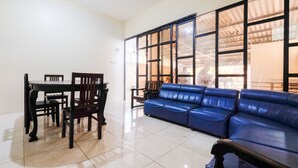 A living room with a blue sofa, a dining table with chairs, and a large window with a view of the outside. - RedDoorz @ Jalan Setiabudi Semarang (Semarang)