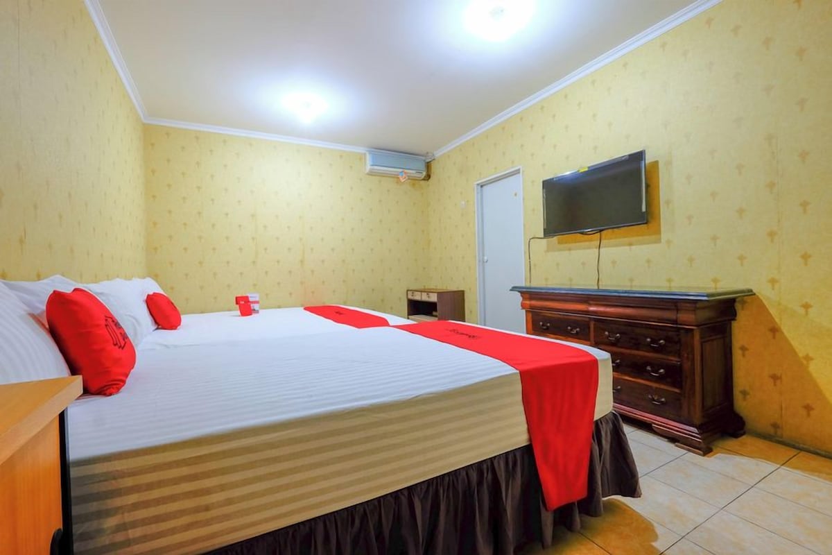 A hotel room with a large bed, a dresser, a television mounted on the wall, and a door.