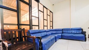 A room with a blue leather sofa, a wooden bench, and large windows with black frames. - RedDoorz @ Jalan Setiabudi Semarang (Semarang)