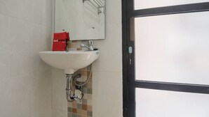 A bathroom with a white sink, a mirror, and a red bag on the counter. - RedDoorz Syariah near Tugu Juang Jambi (Jambi)
