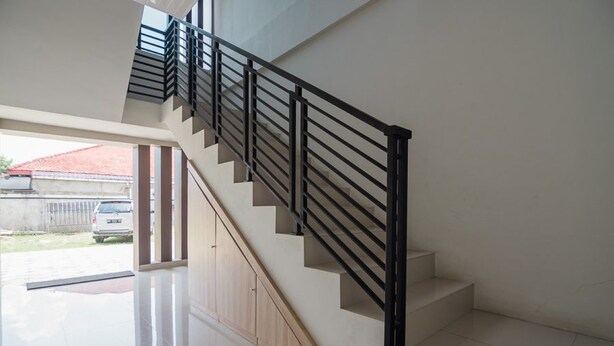 A modern staircase with black railings and wooden steps leading to an open area with a car parked outside. - RedDoorz Syariah near Tugu Juang Jambi (Jambi)