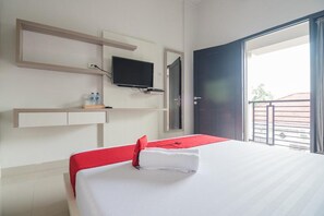 A hotel room with a bed, a TV mounted on the wall, a small shelf with water bottles, and a balcony door. - RedDoorz Syariah near Tugu Juang Jambi (Jambi)