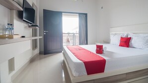 A hotel room with a bed, a TV, a desk with a chair, and a window with curtains. - RedDoorz Syariah near Tugu Juang Jambi (Jambi)