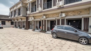 A multi-story building with a tiled courtyard, air conditioning units, and a parked car. - RedDoorz Syariah near Tugu Juang Jambi (Jambi)