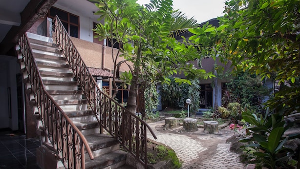A staircase with a wrought iron railing leading to a building entrance, surrounded by greenery and a cobblestone path.