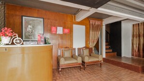 A reception area with a wooden reception desk, two cushioned chairs, a framed portrait, and a whiteboard. - RedDoorz Syariah @ Taman Bendungan Asahan (Jakarta)