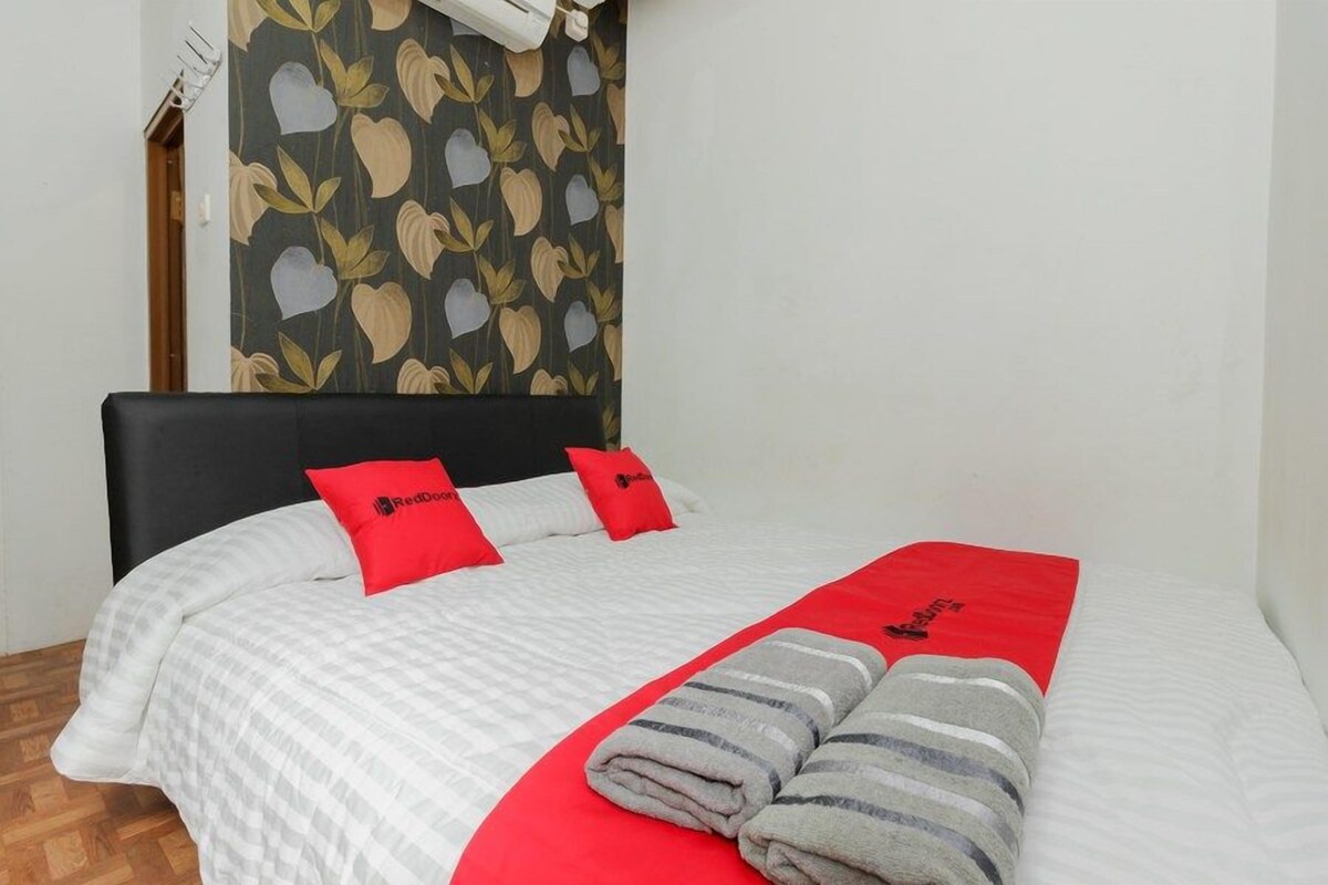 A neatly made bed with a white and red bedspread, two red pillows, and a red blanket with a logo.
