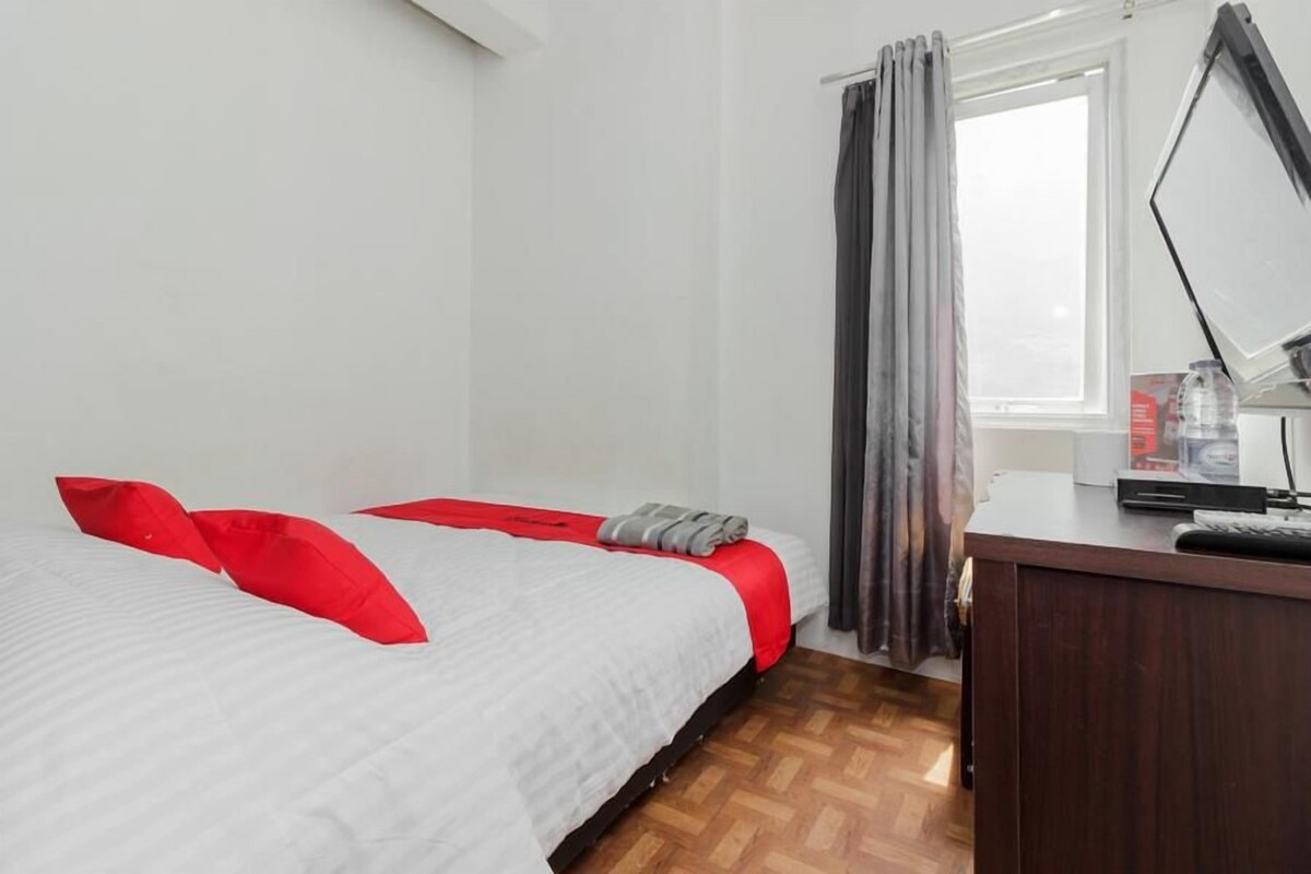A bedroom with a bed, a desk, and a window with curtains.