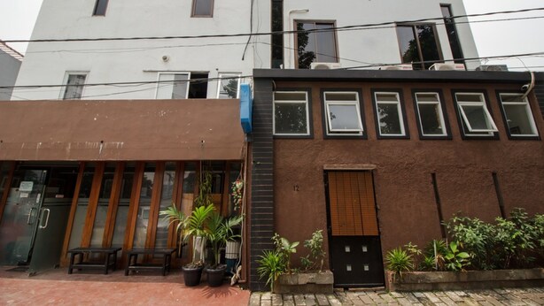 A two-story building with a brown facade and a white upper level. There are potted plants and a small outdoor seating area. - RedDoorz Syariah @ Taman Bendungan Asahan (Jakarta)