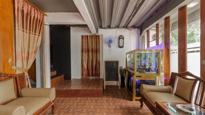 A room with wooden flooring, two sofas, a fish tank, a fan, and a clock on the wall. - RedDoorz Syariah @ Taman Bendungan Asahan (Jakarta)