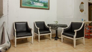 A room with three black and white upholstered chairs, a small round table with a floral tablecloth, and a framed painting of a waterfall on the wall. - RedDoorz Syariah @ Taman Bendungan Asahan (Jakarta)
