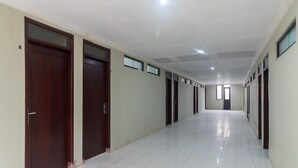 A long, narrow hallway with multiple doors on both sides, tiled floors, and a ceiling with recessed lighting. - RedDoorz near Cikampek Mall Karawang (Karawang)