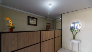 A reception area with a wooden reception desk, a framed artwork on the wall, and a potted plant. - RedDoorz near Cikampek Mall Karawang (Karawang)