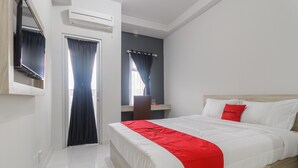 A hotel room with a bed, a desk, and an air conditioning unit. - RedDoorz Apartment @ Dramaga Tower (Ciampia)