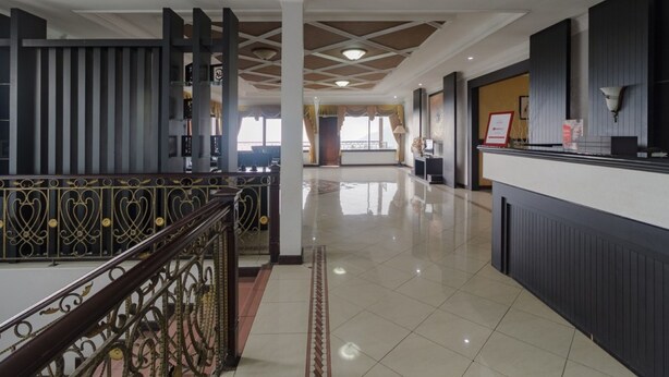 A hotel lobby with a reception desk, a staircase with ornate railings, and a tiled floor. - RedDoorz Syariah @ Cipanas (Cipanas)