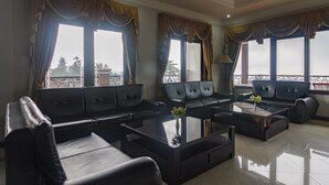 A spacious living room with a modern sofa set, a glass coffee table, and large windows with curtains. - RedDoorz Syariah @ Cipanas (Cipanas)