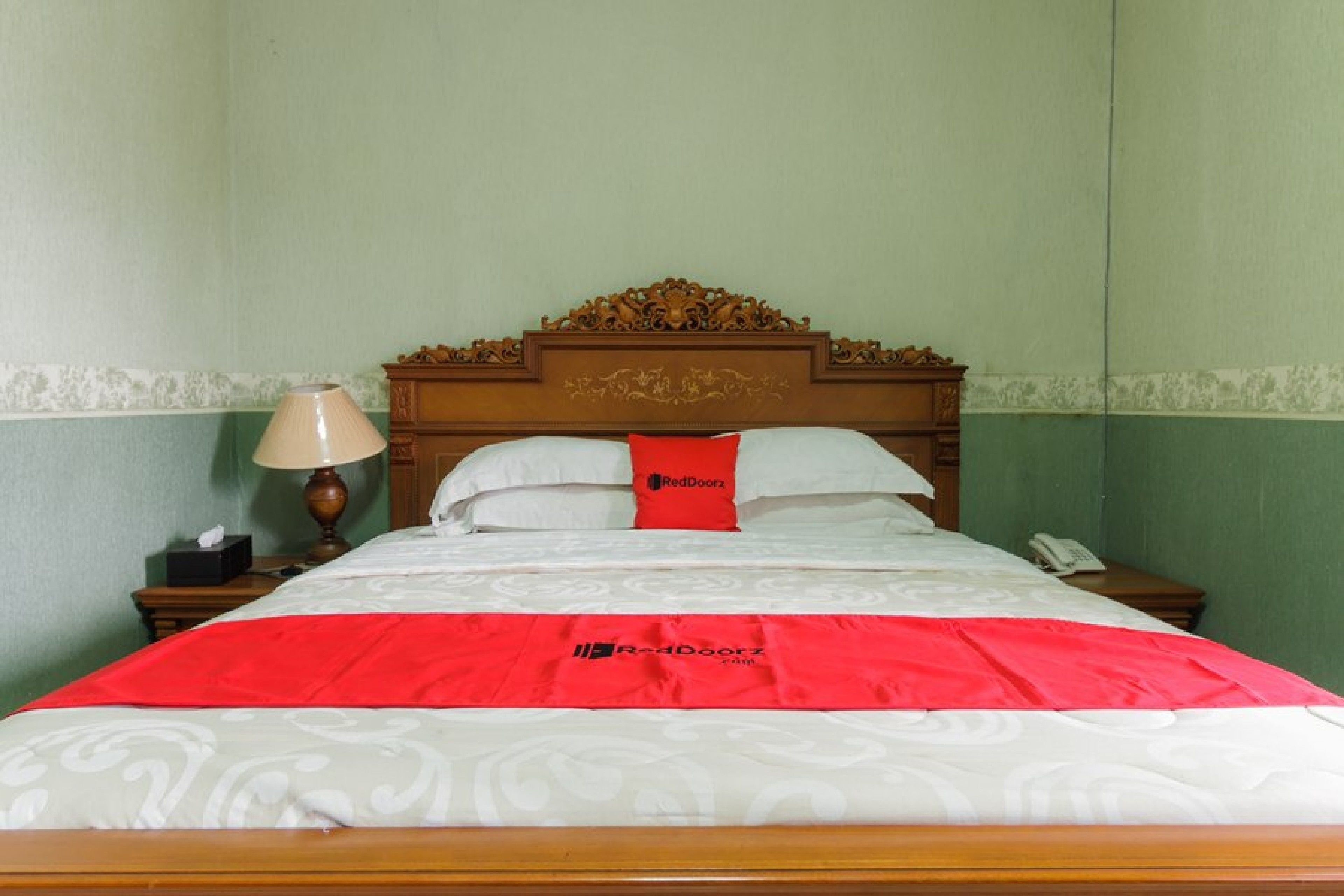 Un letto ben rifatto con copripiumino rosso e bianco, una testiera in legno e una lampada su un comodino.