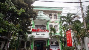 A hotel with a green and white facade, a signboard with 'RedDoorz' and 'Hotel Grupo Kullio' written on it, and a parked car in front. - RedDoorz @ Genteng Surabaya 2 (Surabaya)
