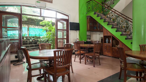 A restaurant with wooden furniture, a green staircase, and a view of the outdoors. - RedDoorz @ Genteng Surabaya 2 (Surabaya)