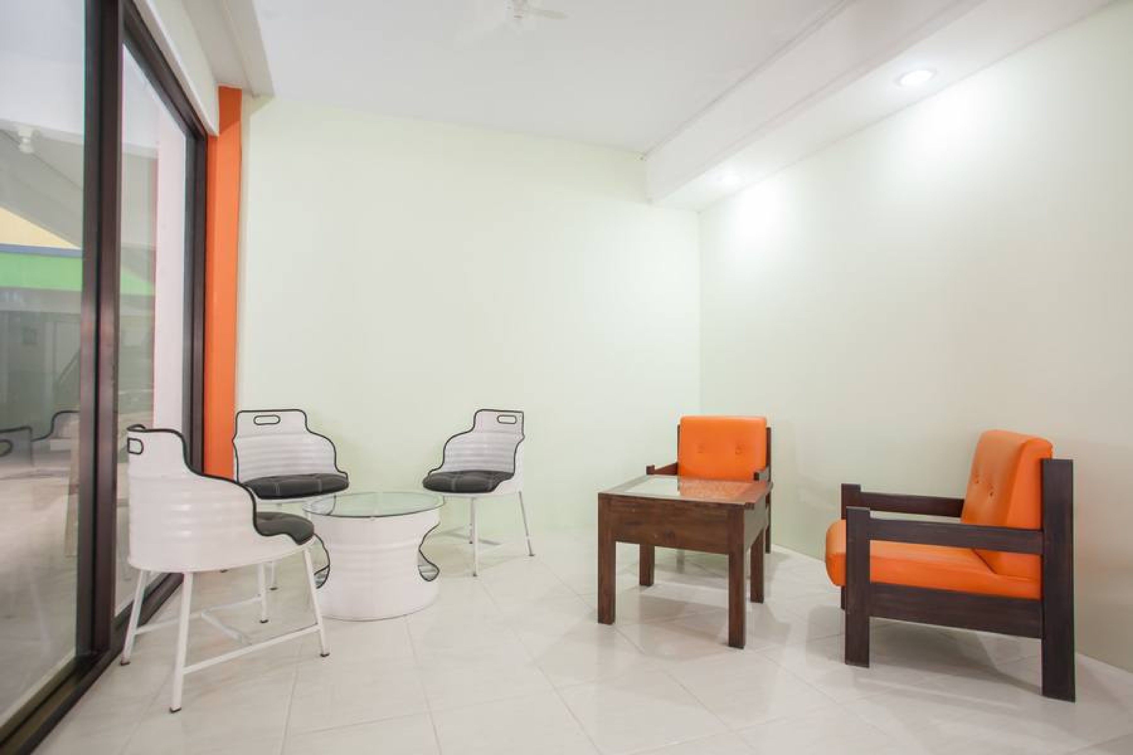A room with a glass table, two white chairs, an orange chair, and a wooden table.