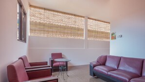 Ein Zimmer mit einem roten Sofa, einem kleinen roten Sessel, einem kleinen runden Tisch und einem Fenster mit einem gemusterten Rollo.