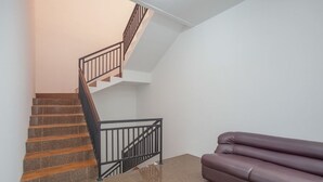 Eine Treppe mit schwarzer Metallstange, ein braun gefliestes Podest und ein violettes Sofa in einem Raum mit weißen Wänden.