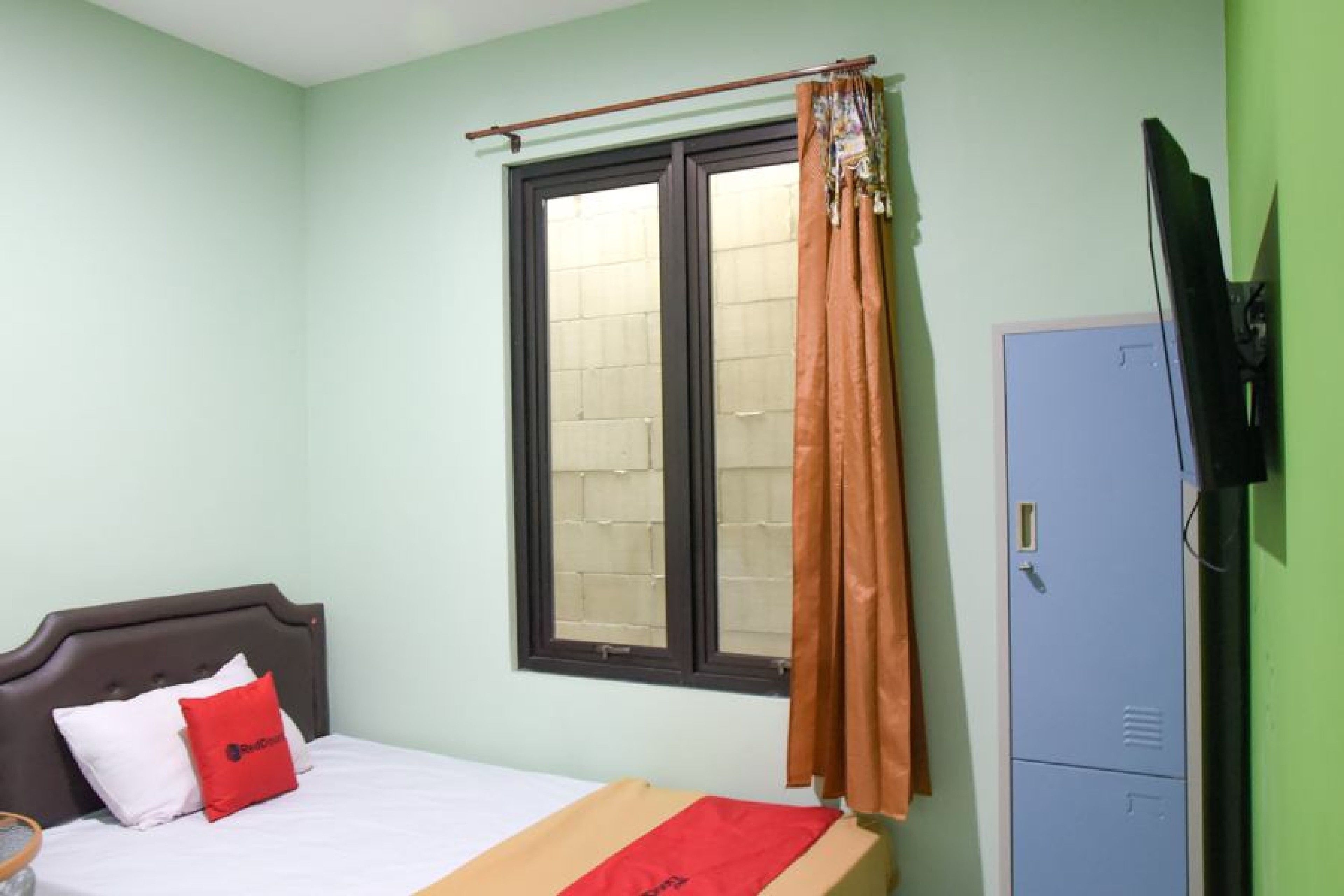 A bedroom with a bed, a window with curtains, a wardrobe, and a television on the wall.