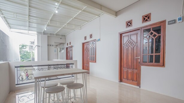 A spacious room with a long table and four stools, a large wooden door with intricate designs, and a balcony with a metal railing. - RedDoorz near Ciputra Golf Surabaya (Surabaya)