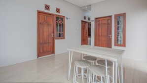 A room with a wooden door, a white table with stools, and a light-colored floor. - RedDoorz near Ciputra Golf Surabaya (Surabaya)