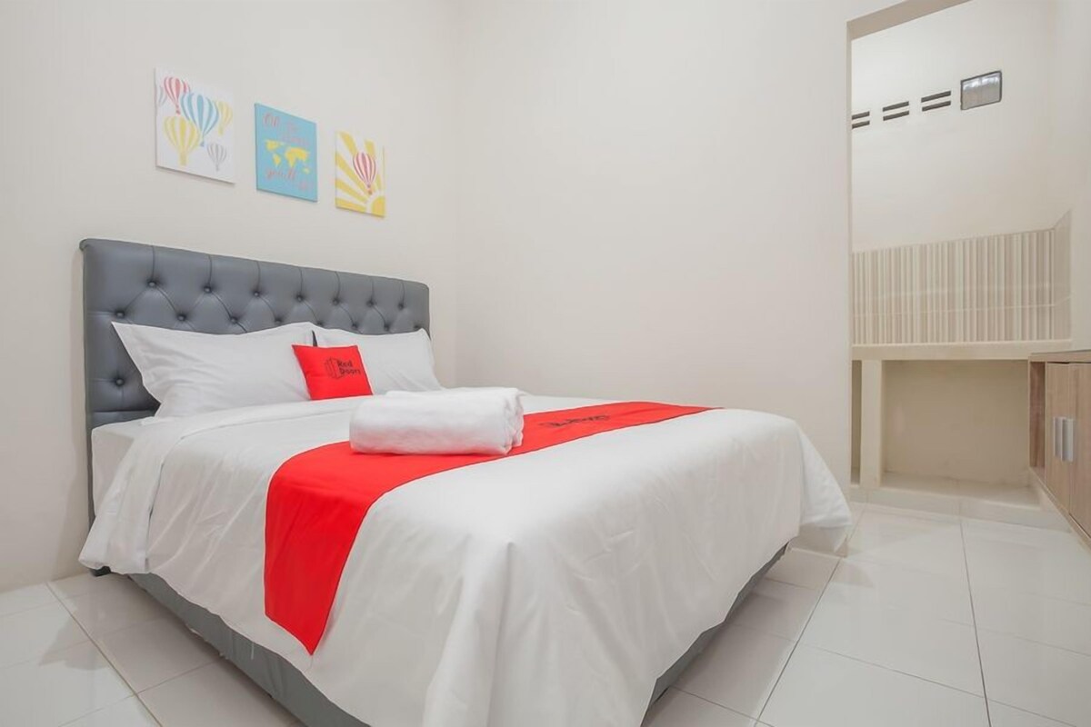A hotel room with a bed, white and red bedding, a grey headboard, and artwork on the wall.