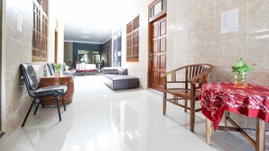 Um saguão de hotel com piso lustroso, uma mesa de madeira com toalha vermelha, um sofá e uma cadeira.