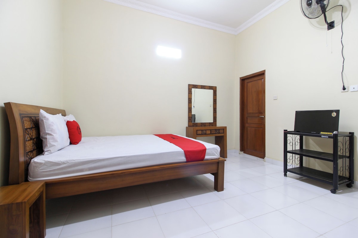 A bedroom with a wooden bed, a bedside table, a mirror, a wardrobe, and a desk with a chair.