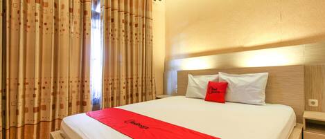 A hotel room with a neatly made bed, a red bedspread, and a curtain with a geometric pattern.
