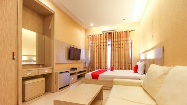 Quarto de hotel com cama, televisão, escrivaninha e uma pequena cozinha.