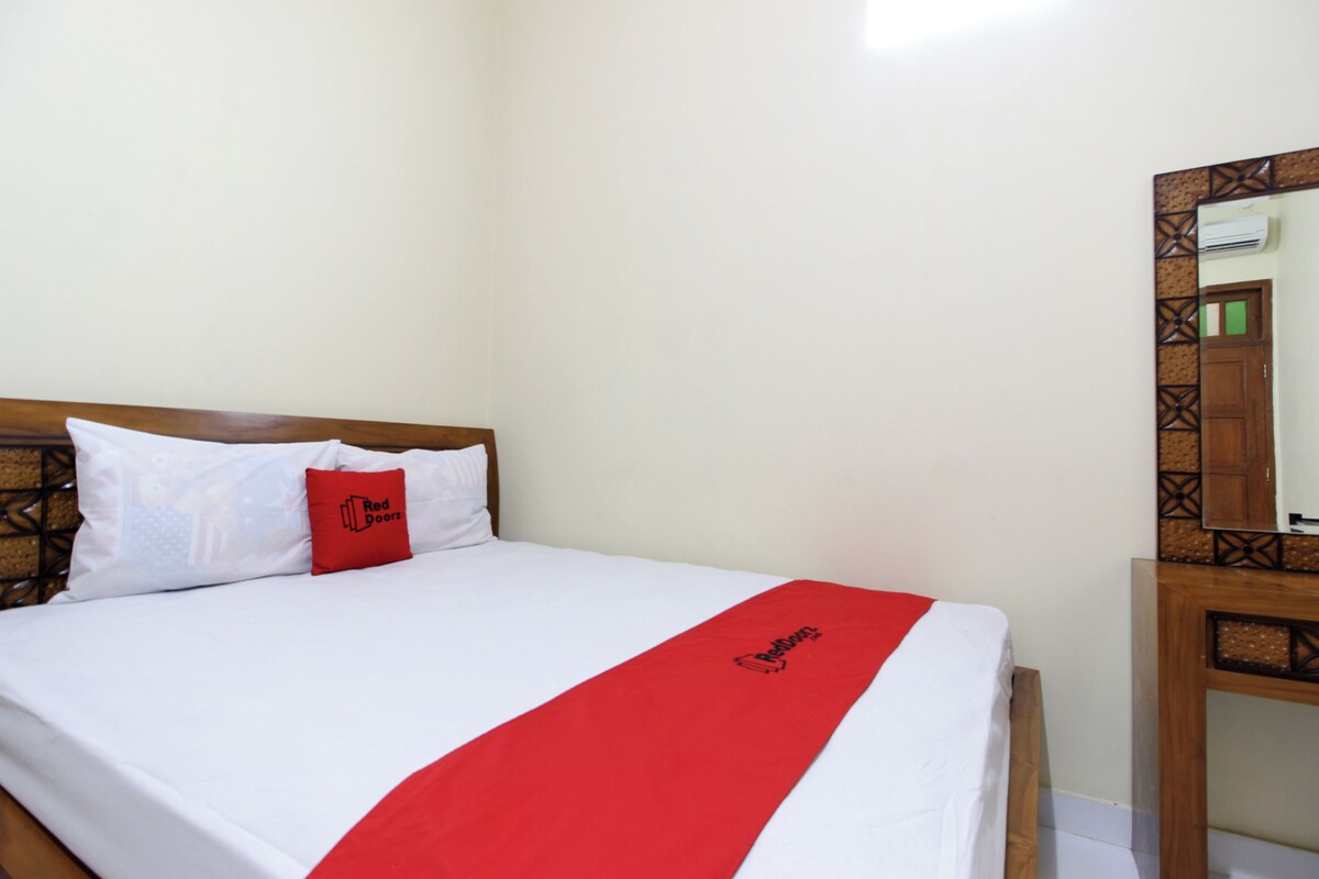 A neatly made bed with a white and red bedspread, a red pillow with the text "Red Doors," and a wooden headboard.