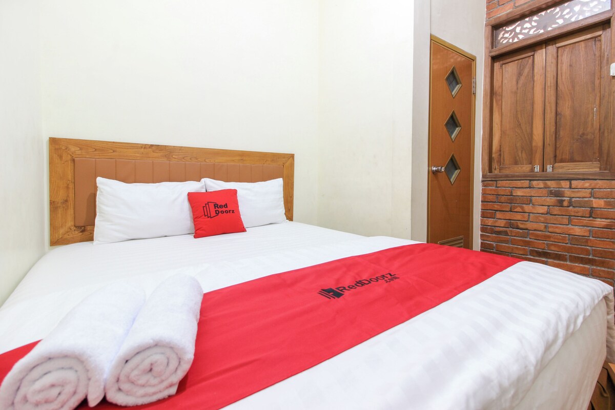 A neatly made bed with white and red bedding, a red pillow with text, and a wooden headboard.