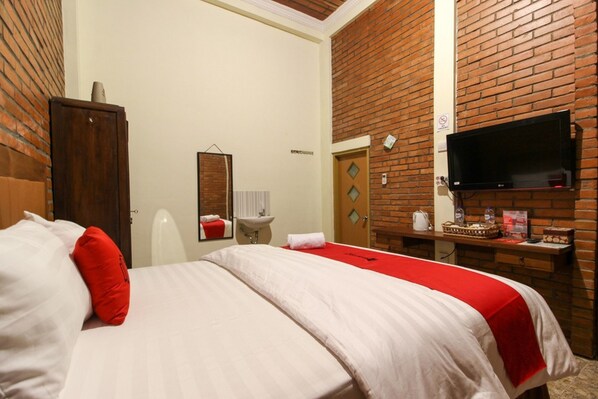 Una habitación de hotel con cama, televisor montado en la pared, pared con diseño de ladrillo y armario de madera.