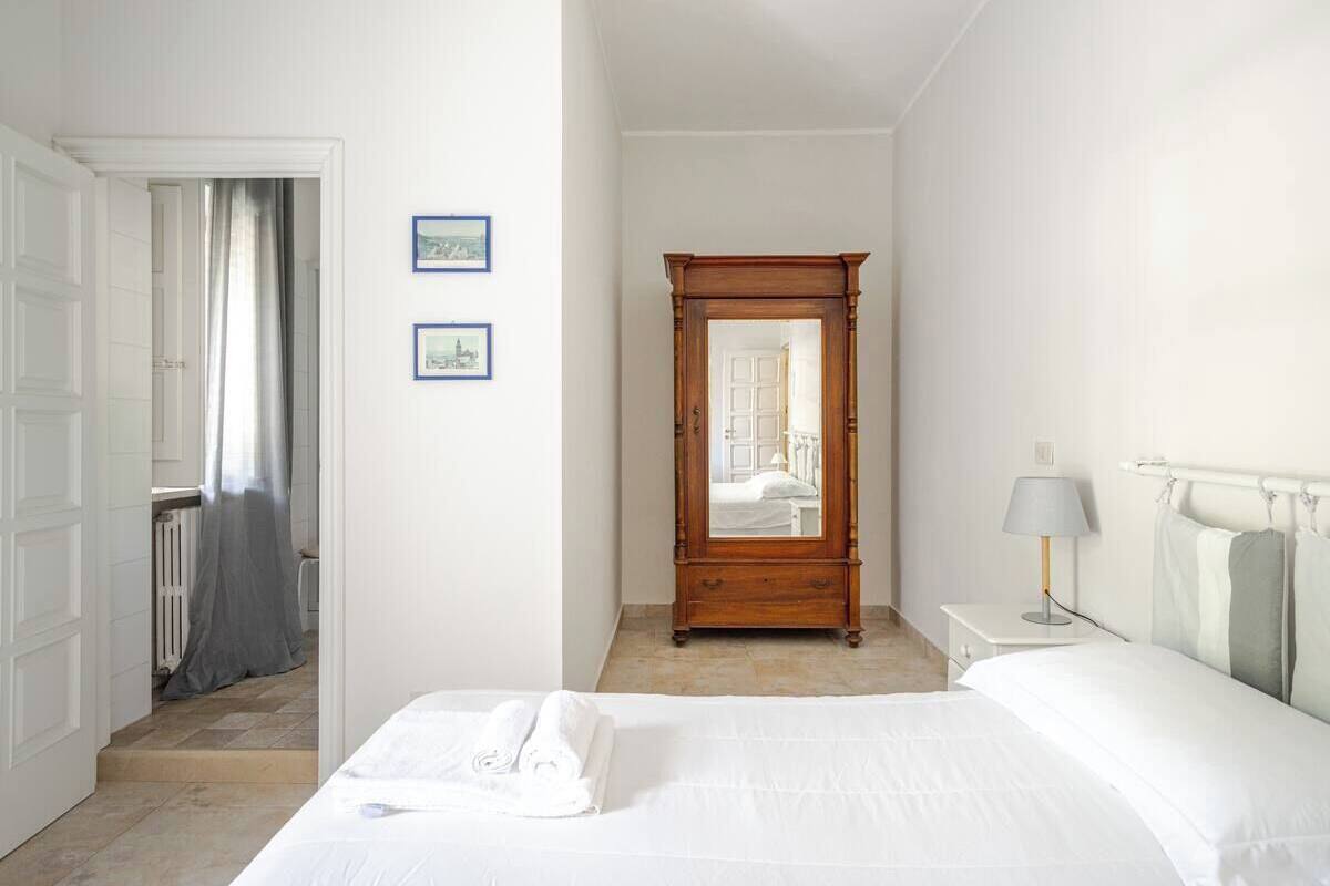 Habitación de hotel con cama, mesita de noche con lámpara, armario de madera y dos cuadros en la pared.